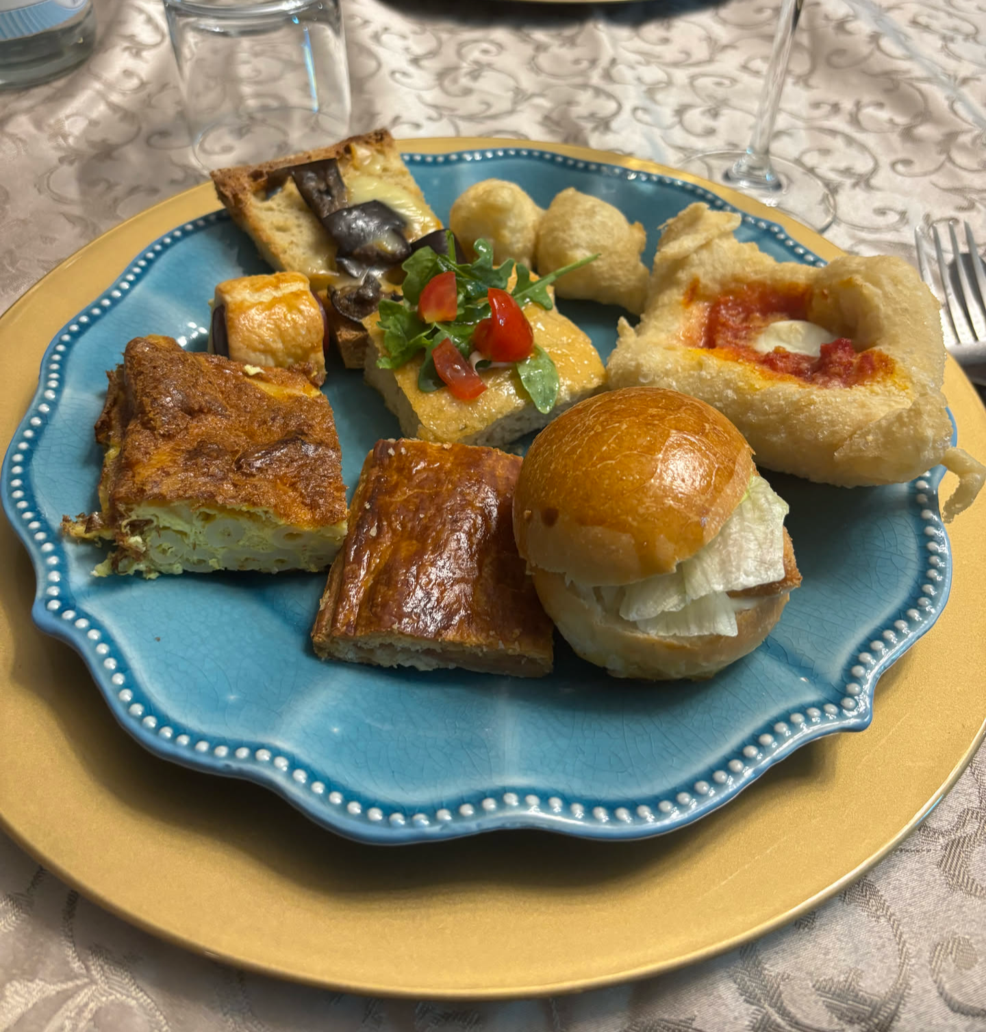 A colorful plate with assorted appetizers, including a small sandwich, baked goods, and garnished vegetables.
