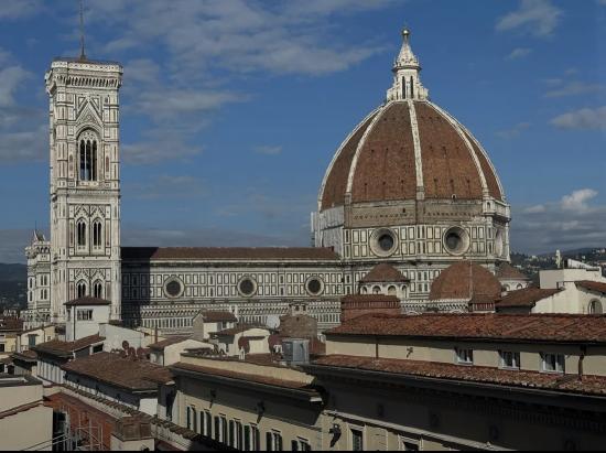 View of Florence's iconic cathedral, featuring its large dome and adjacent campanile under a blue sky.