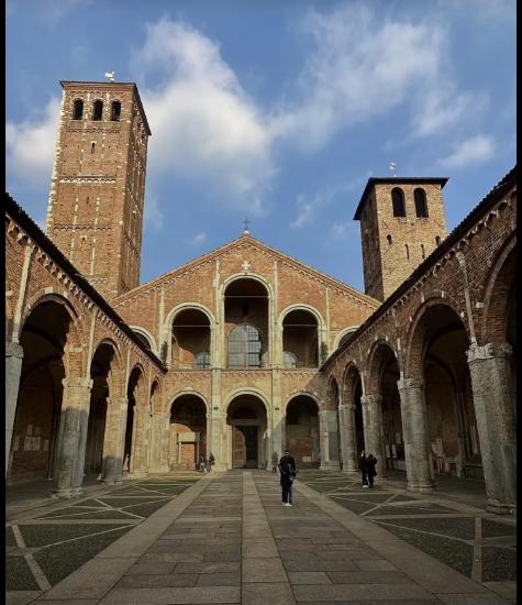 Interior view of a historic brick building with two towers, arched colonnades, and people walking on a stone pathway.