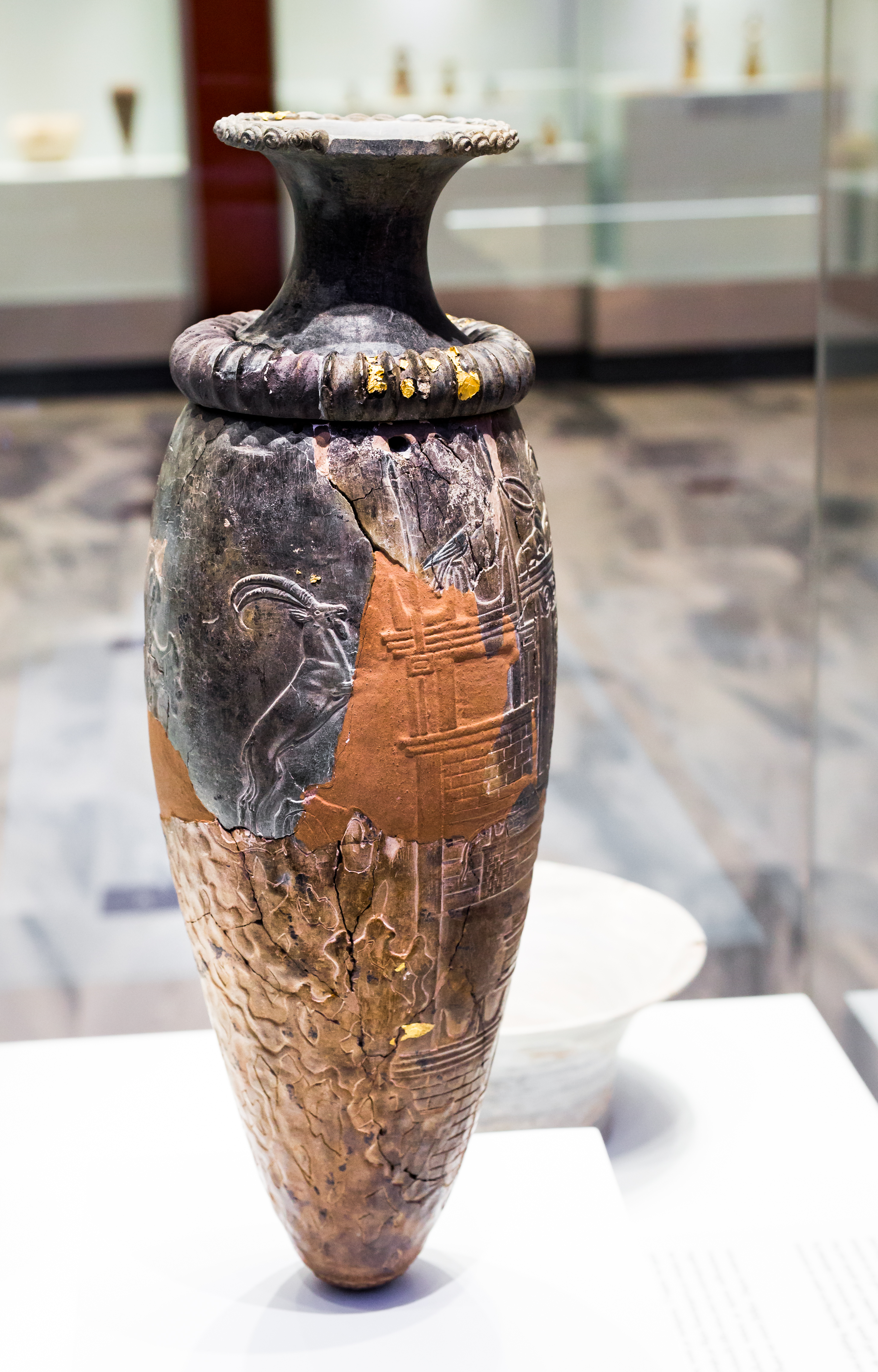 Ancient vase with intricate carvings and a two-tone finish, displayed in a museum setting.
