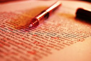 Photo of uncapped red pen laying on a typed page, which has proofreading marks on it