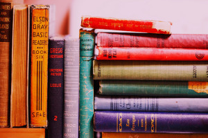 Photo of brightly colored vintage books. Those on the left are standing vertically, while those on the right are lying stacked horizontally