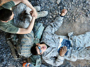 Photo looking down on a US Marine in fatigues lying on the ground with an open copy of the book Middlesex open on his chest. Another Marine sits near his head, with his knees to his chin.