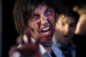 Foto de persona con maquillaje zombie, gruñendo y extendiendo la mano hacia la cámara