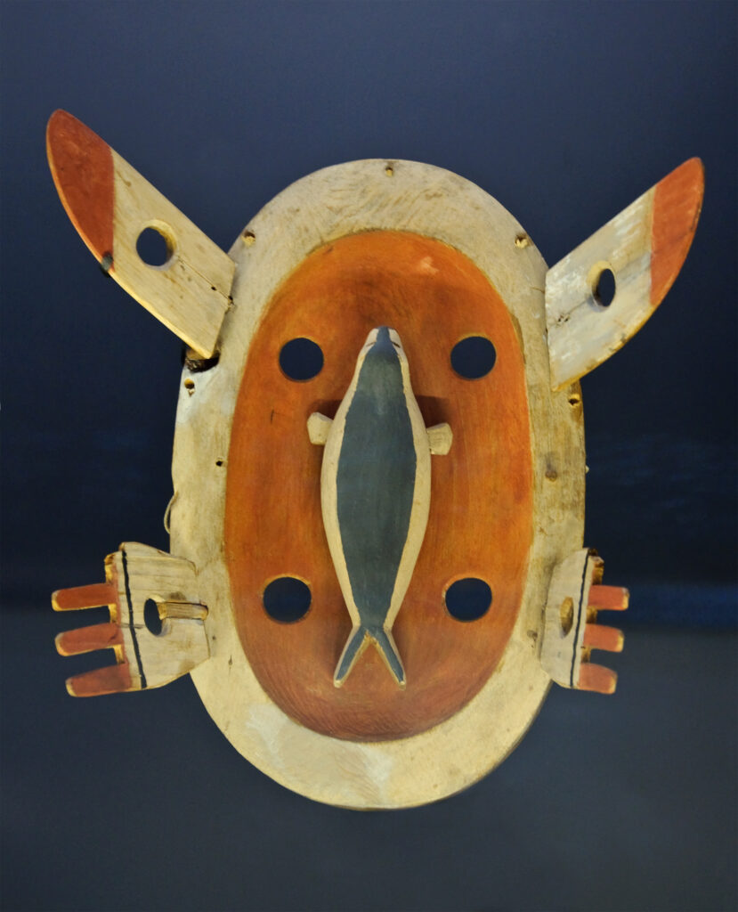 Yup'ik masks are used in ritualistic dances by Shamans to connect the natural and spiritual worlds. This mask is in a yellow wood with the figure of a seal, a traditional food for the Indigenous people of Alaska and what appears to be hands and ears that protrude outward.