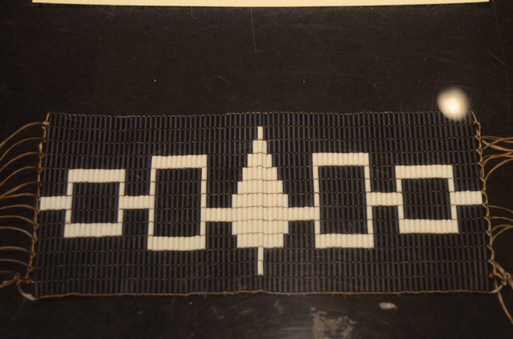 This belt, known as the Hiawatha Belt, symbolizes the unity of the five original Haudenosaunee nations. The belt is made of dark blue color leather and it is decorated with traditional shell beads or wampums used by many Eastern Woodlanders. Each tree or square is made of wampums and represents a tribe of the original five nations, and the line connecting them represents the path of peace. 