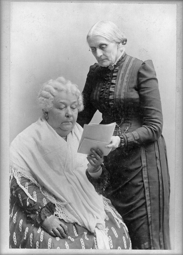 Photograph of Susan B. Anthony (standing) and Elizabeth Cady Stanton (seated) together reading documents. [Elizabeth Cady Stanton, seated, and Susan B. Anthony, standing, three-quarter length portrait], between 1880 and 1902. Library of Congress.