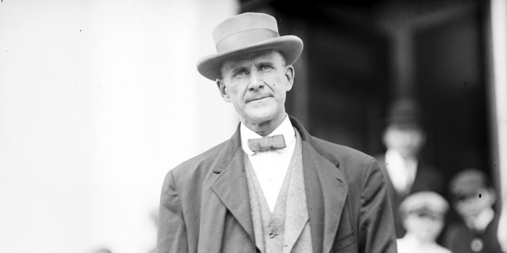 A man in a suit and hat stares into the distance.