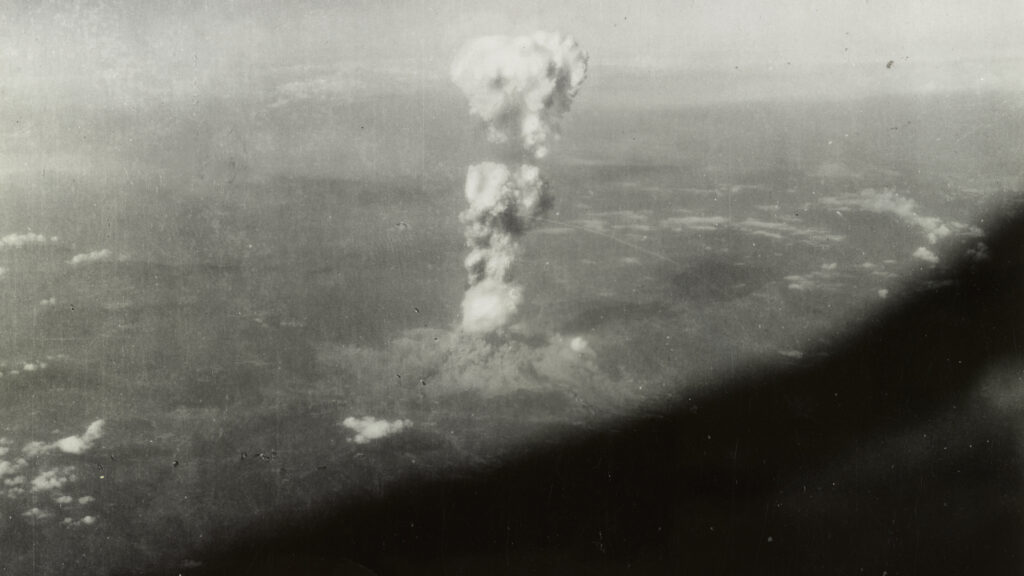 A mushroom cloud rises far in the distance.