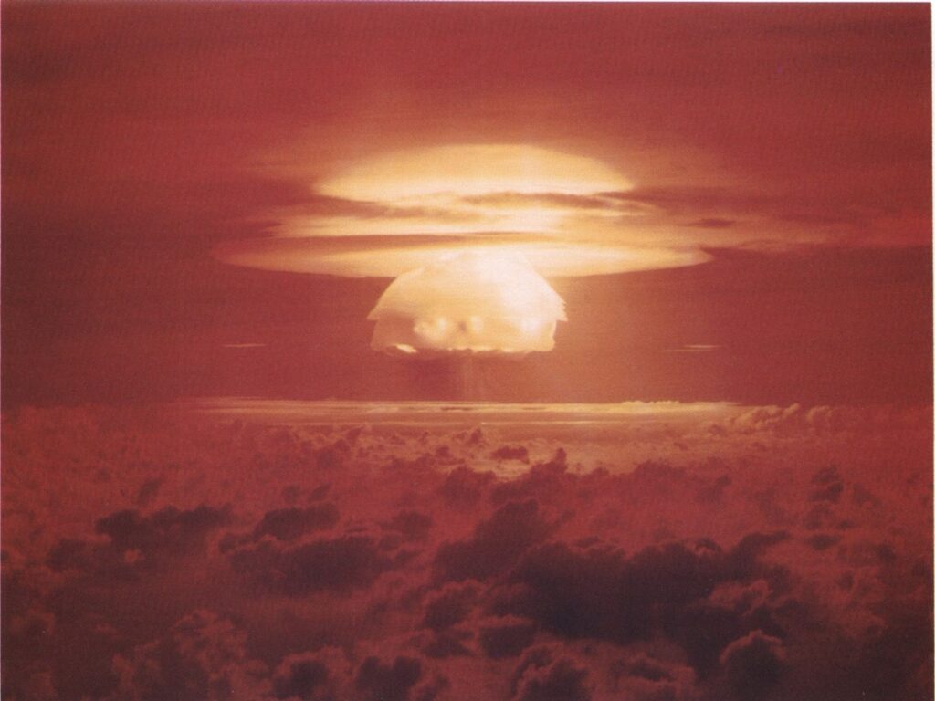 A large mushroom cloud rises in the distance.