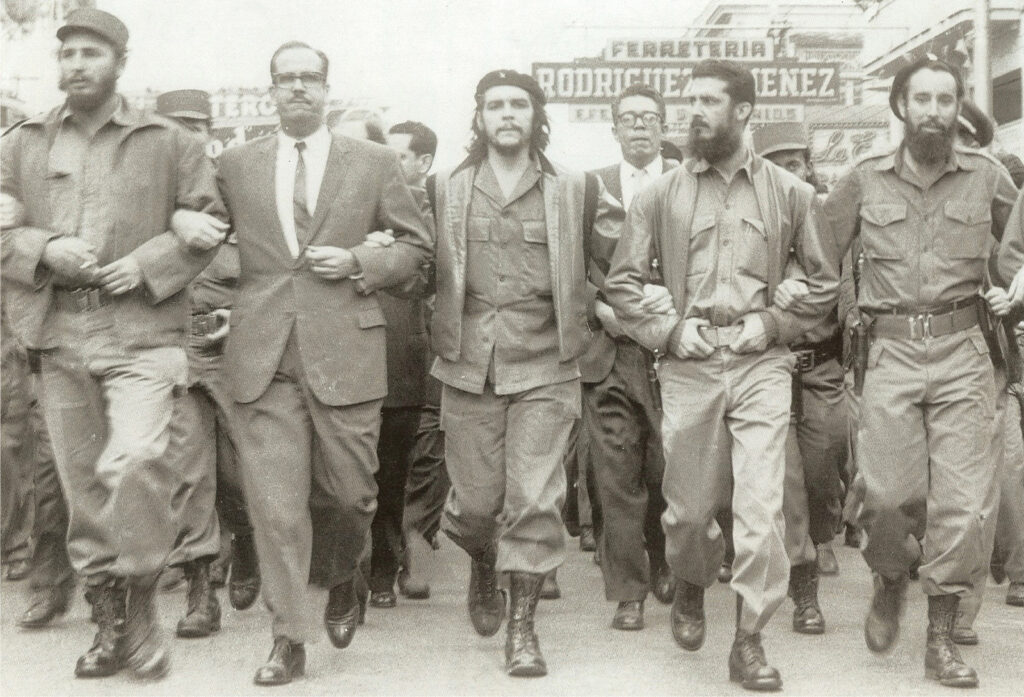 Five men, four in fatigues and one in a suit, march, arm in arm, down a city street.