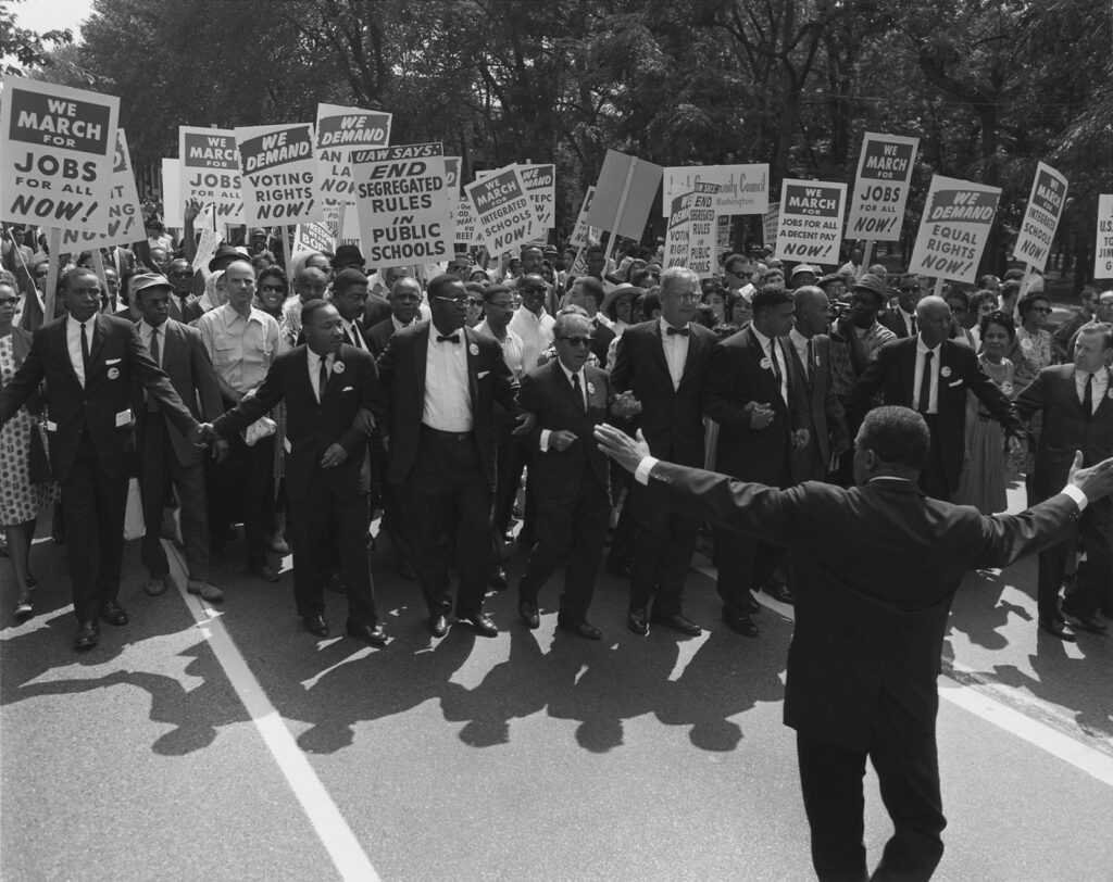 Men and women demonstrate. The placards advocate for jobs, voting rights, and an end to segregation.