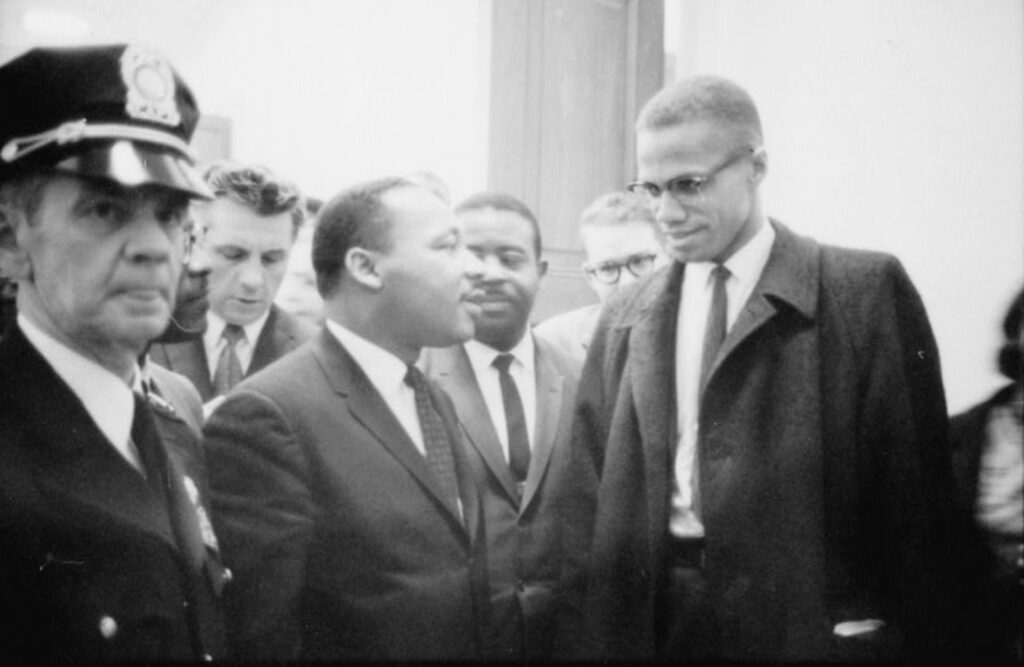 Two men stand next to each other and appear to speak amid a crowd.