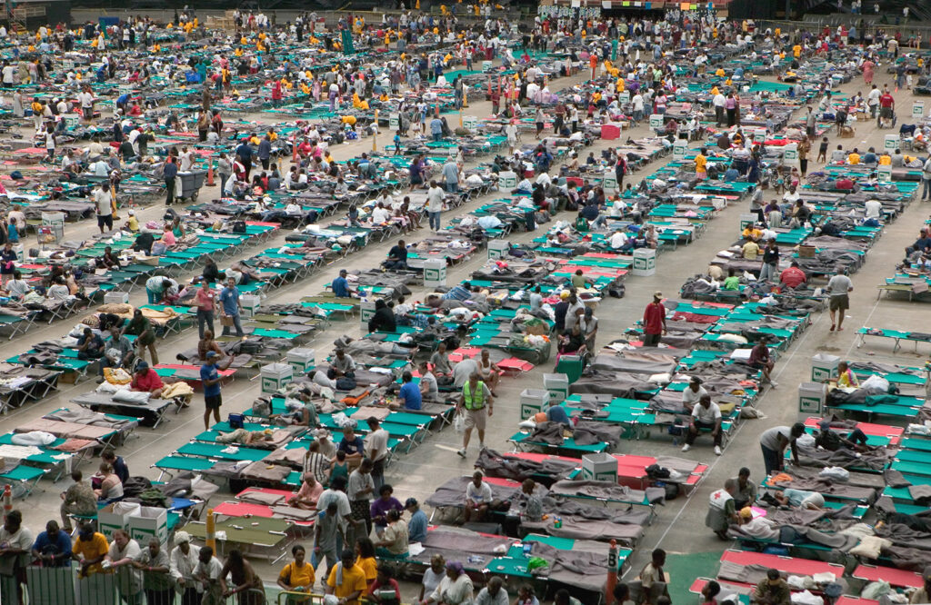 Crowds mill around a large surface with hundreds of cots.