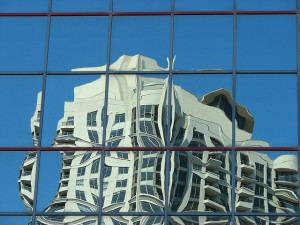 Foto de las ventanas exteriores espejadas de un edificio, que presentan un reflejo desarticulado y deformado de un edificio al otro lado de la calle