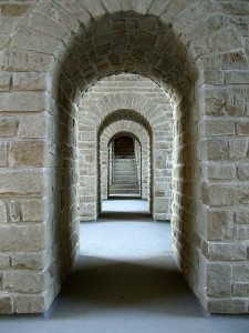 Foto mirando hacia abajo por un pasillo abierto, mostrando una serie de arcos de piedra que conducen a un conjunto de escaleras en la distancia