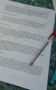 Typed page of text with "Draft" watermarked across it. A red pen rests on it, and red marks are all over the page.
