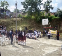 A school assembly outdoors, on a dirt basketball court