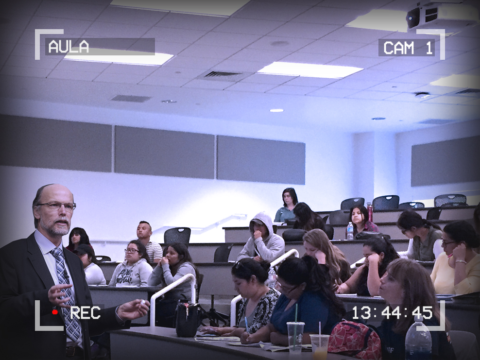Image of a lecture hall. A professor is lecturing. Text around the outside of the image reads: Aula, Cam 1, 13:44:45. A red dot signifies recording.