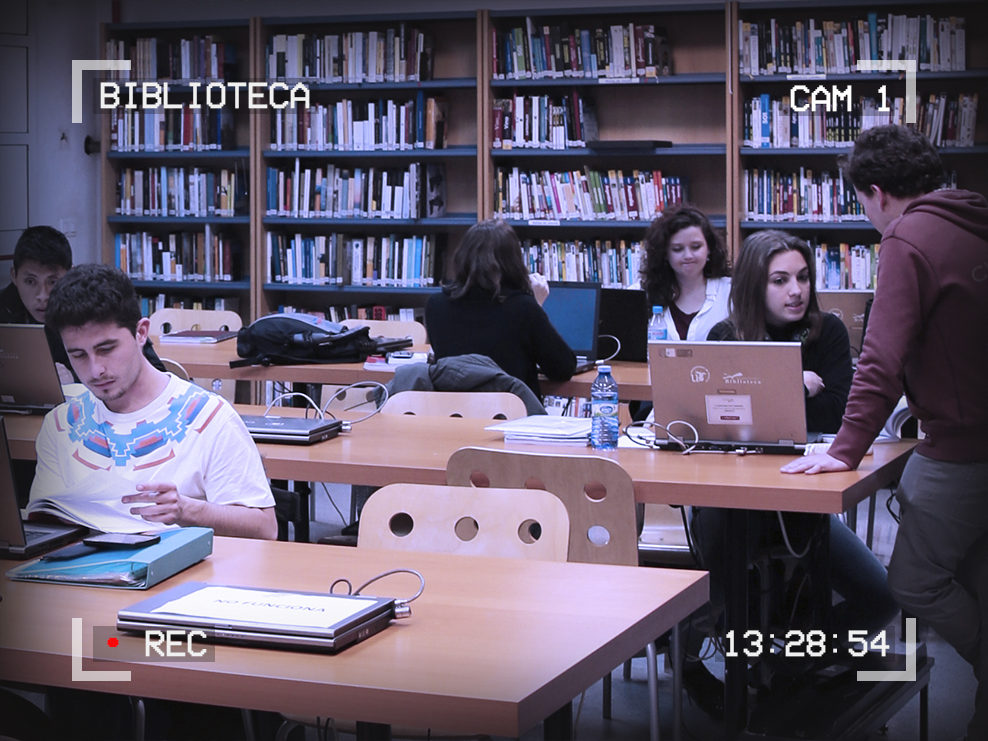 Photo of students working in a library. Text around the outside of the image reads: Biblioteca, Cam 1, 13:28:54, Recording