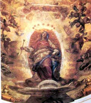 The Virgin Mary being lifted to heaven. She is standing in the clouds with the moon at her feet. There is a halo of stars around her head, and sunlight pours from the clouds above her head. She is flanked on both sides by angels.