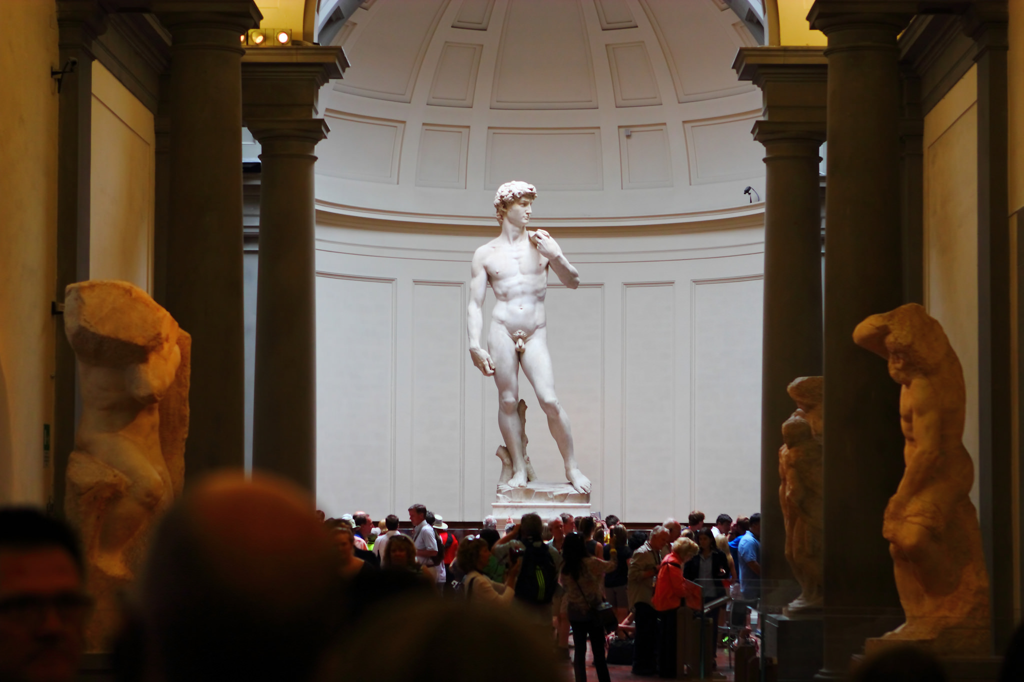 El David de pie en una gran sala circular. La estatua está levantada sobre un pedestal, por lo que no es obstruida por la gran multitud reunida frente a ella.