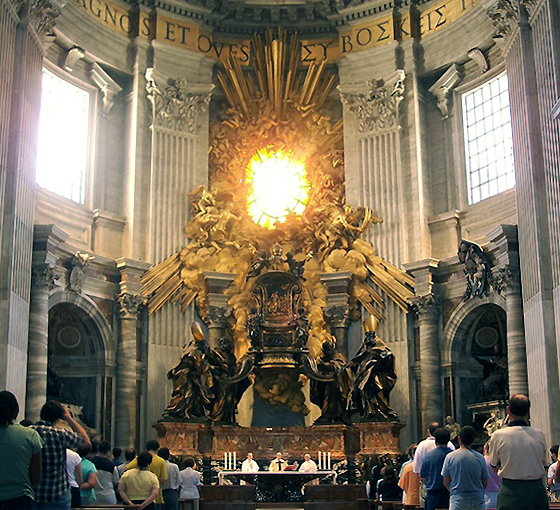 The chair of St. Peter is ornately carved and raised above the congregation and clergy in the church. It is made to larger than life proportions. It is surrounded by gold and wooden representations of clouds, saints, and sunlight. There is a window in the center of the gilding above the chair. The sun is caught in the window.