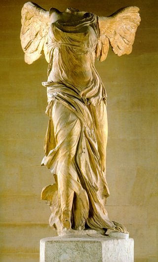 Una escultura de mármol de una mujer alada. Con el tiempo, se le han perdido la cabeza y los brazos. Sus ropas drapeadas aparecen ligeras y fluidas, a pesar del duro medio de la escultura.