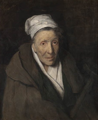 An elderly woman with a white cloth covering her hair. She wears a heavy brown coat over white clothes. The coat seems old and too large for the woman.