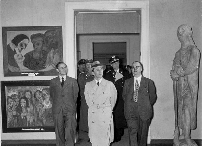 El Dr. Goebbels y un grupo, incluido un equipo de seguridad, recorren la exhibición.