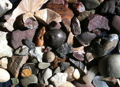 A variety of stones with differing colors, textures, and sizes. Overall the color pallet is muted, but there are some brighter reds and greens.