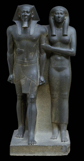 Stylized statue of a man and a woman standing next to one another. Both are very static. The rock between the two Figures has not been removed to give the statue stability
