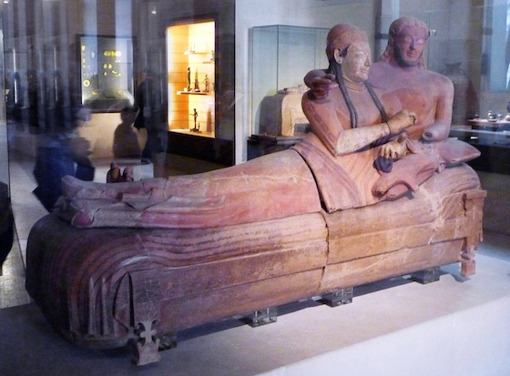 A sarcophagus adorned with a sculpture of a man and a woman lounging with one another on top of the sarcophagus.