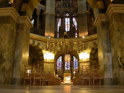 The interior has vaulted ceilings and all surfaces are made of polished stone. The photograph is angled at an alcove. There are stained glass windows in the rear of the alcove.