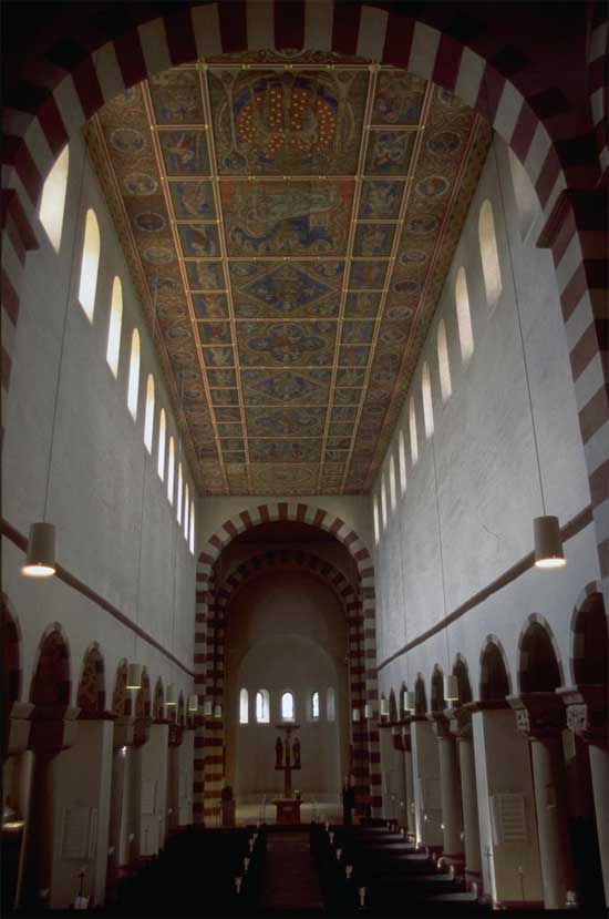 There is a long narrow space leading to an alcove. The ceilings are vaulted, with a row of windows just below the ceiling. The ceiling has worked stone creating an artistic and geometric pattern.