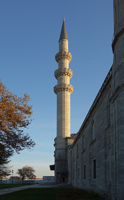 A simple minaret. There are three rings of balconies and the minaret is topped with a pointed blue roof.