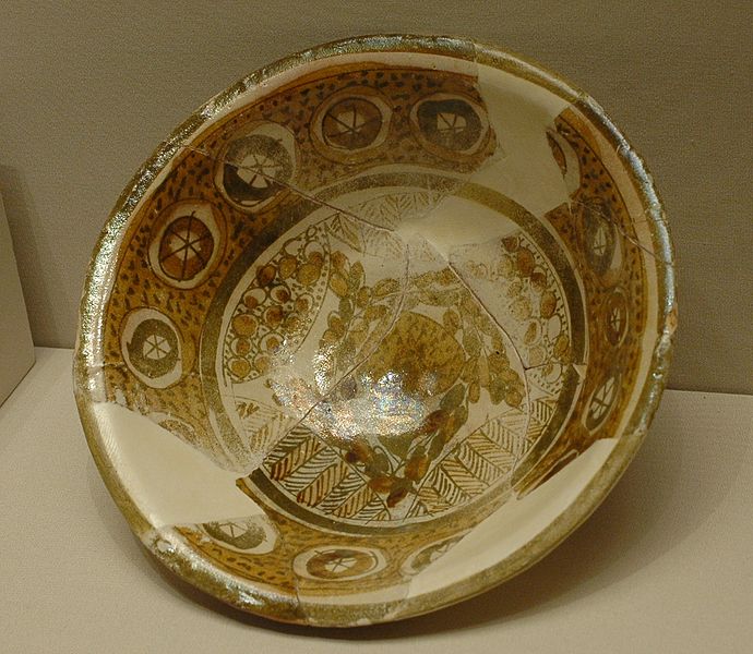 A broken bowl has been placed back together. The edges of the bowl have repeating circles, and the bottom of the bowl has a more intricate drawing on it.