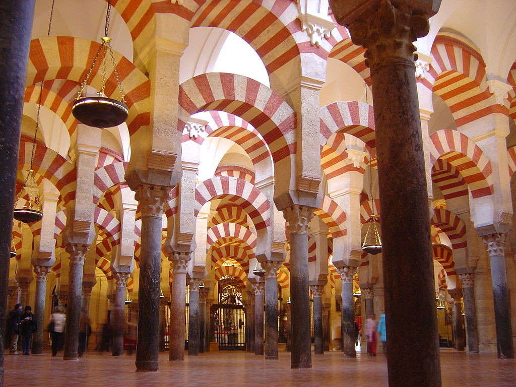A hall filled with archways. Each archway is curved and painted with nearly vertical stripes. These repeated stripes give the room a sense of extending into a further space.