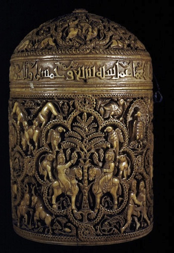 A cylindrical shape with intricate designs on the body and the lid. There is a band with writing between the two sections.