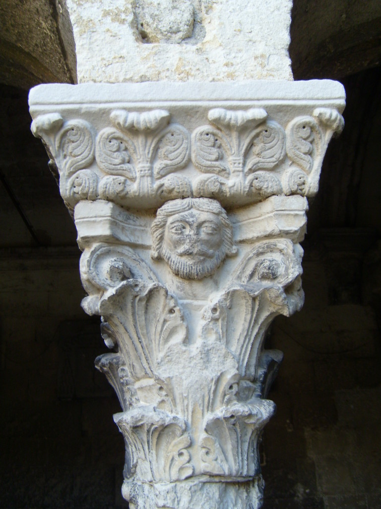The capital features leaf patterns. There is also a face, worn away from time, just below the capital.