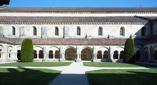 The exterior of the abbey has several archways leading to an open air walkway. There is a second level above this. The grounds are well kept with paved walkways.