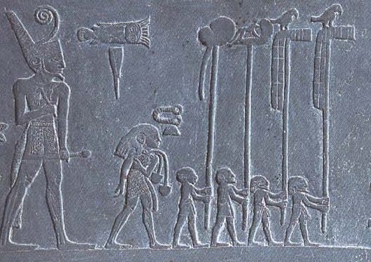 Fotografía de tablilla de piedra. Representa seis figuras talladas en la piedra. Parecen estar caminando en la fila. La cifra más grande se encuentra al final de la línea, cada figura al frente es progresivamente más pequeña.