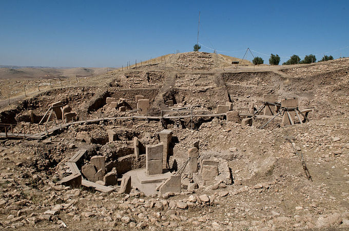 Fotografía representa ruinas de Göbekli Tepe. La foto presenta un montículo de tierra y roca con los restos de pilares y losas que alguna vez formaron una estructura sagrada.