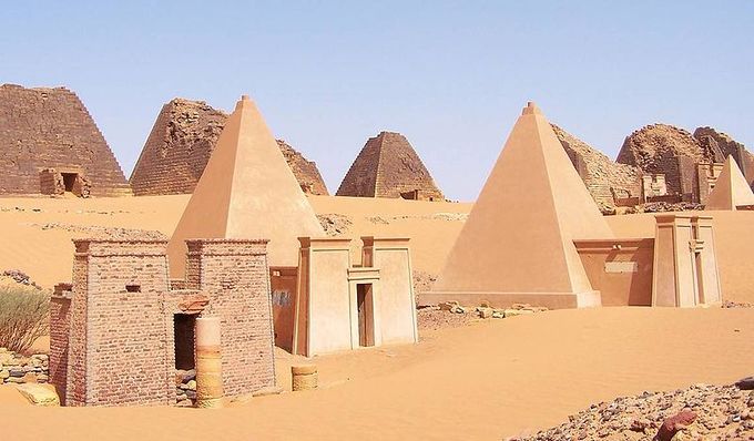 Photo depicts pyramids in the desert of Sudan. They hey are built of stepped courses of horizontally positioned stone blocks. They are tall, narrow structures with a 70-degree incline.