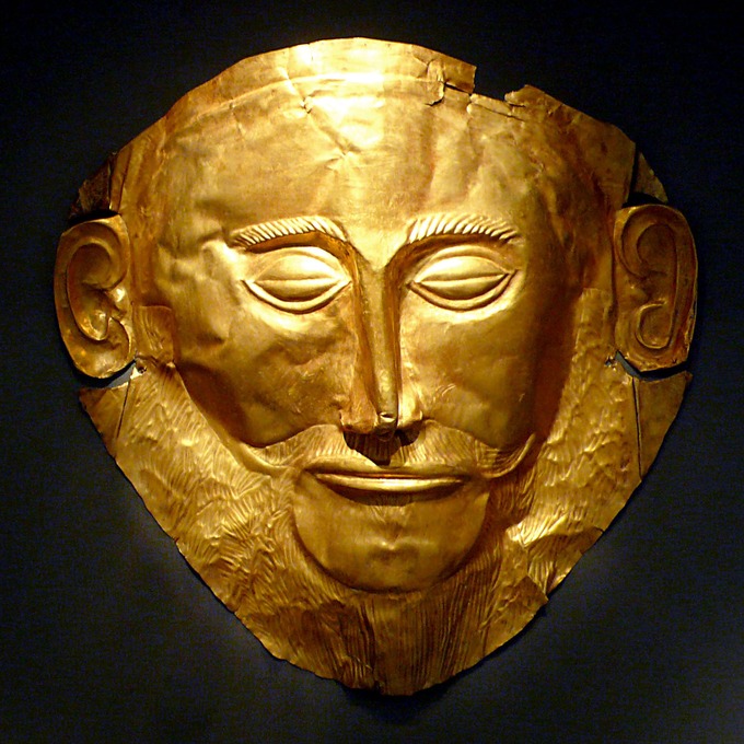 This is a color photo of a gold mask depicting Agamemnon's face. His eyes are closed and his brows are thick and prominent. He has a thin, narrow nose and a moustache.