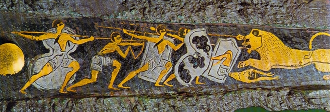 Color photo of hunting dagger with a scene depicting a lion hunt. Several hunters holding spears and shields are approaching a lion with its mouth open and its teeth bared.