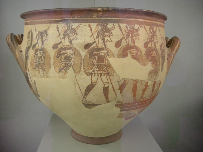 Color photo of terracotta vase decorated with warriors wearing armor holding spears or staffs.