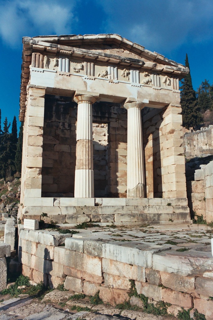 This is a color photo of the current-day exterior of the Athenian Treasury in Delphi, Greece. It is a columned structure with marble pillars.