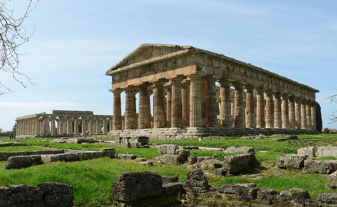 This is a color photograph of the Temple of Hera II and Temple of Hera I, in Paestum, Italy. It shows the columns and foundations of the structures.