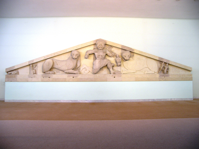 Photo of pediment depicting Medusa in a formulaic, stylized fashion. There are two snakes wrapped around her waist like a belt. She is flanked by panthers.